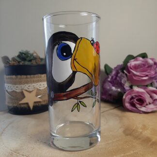 Verre haut peint à la main représentant un toucan avec un grand bec jaune et une petite coccinelle rouge posée dessus, création artisanale Aleco.