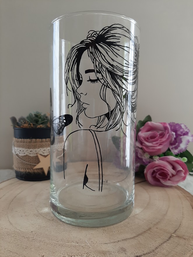 Vase cylindrique en verre transparent avec le profil d'une jeune femme aux yeux clos et un papillon posé sur son épaule, peint à la main à l'encre noire, artisanat Aleco.