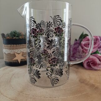 Pichet en verre transparent avec anse, décoré de volutes baroques noires et de petites fleurs bordeaux et vertes peintes à la main, artisanat Aleco Vendée.
