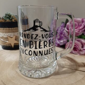 chope de bière en verre transparent avec anse, décorée d'une illustration de montagne surmontée d'une chope et de l'inscription humoristique "RENDEZ-VOUS EN BIÈRES INCONNUES", artisanat Aleco.