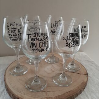 Série de verres à vin à pied en verre transparent, chacun décoré d'une phrase humoristique différente peinte à la main en noir et rouge, comme "Si tu veux t'amuser vin chez moi", artisanat Aleco.