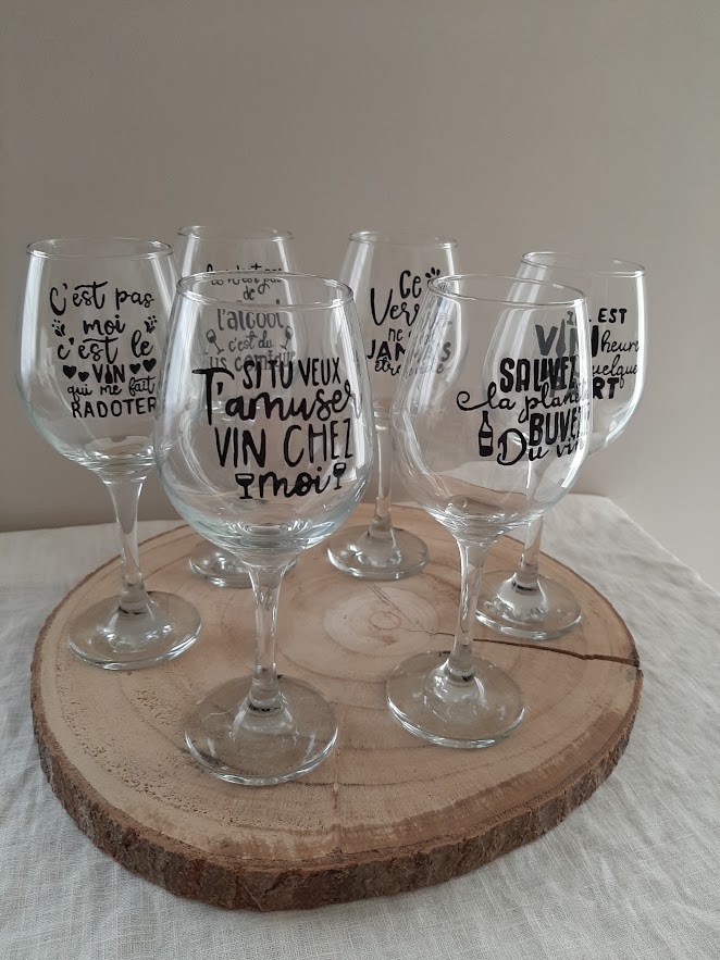 Série de verres à vin à pied en verre transparent, chacun décoré d'une phrase humoristique différente peinte à la main en noir et rouge, comme "Si tu veux t'amuser vin chez moi", artisanat Aleco.