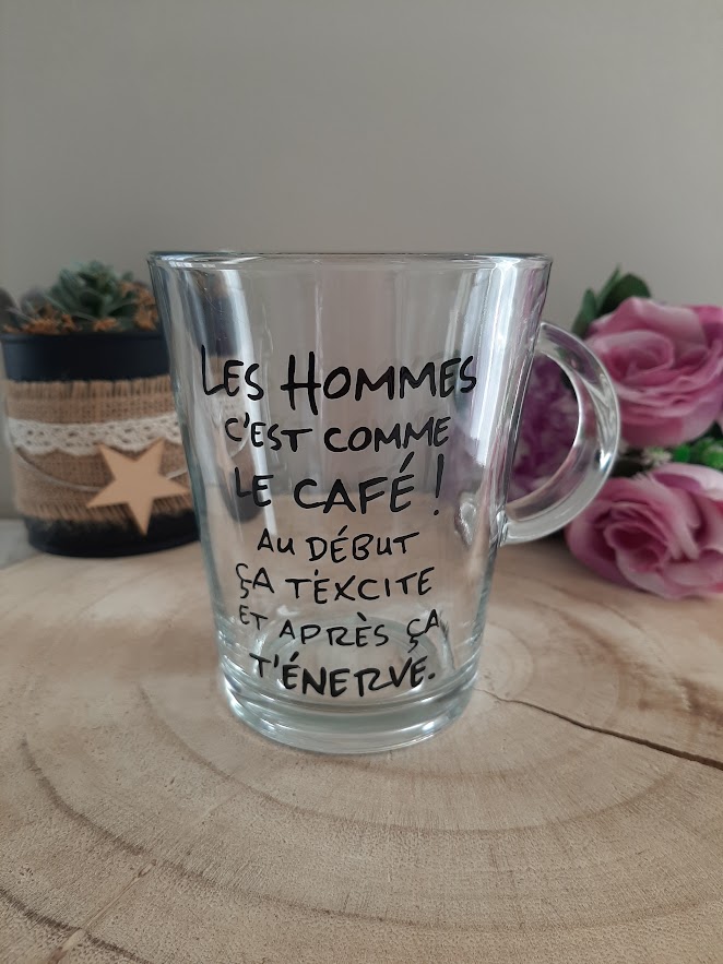 Mug en verre transparent avec anse, décoré d'une citation humoristique peinte à la main en noir : "LES HOMMES C'EST COMME LE CAFÉ ! AU DÉBUT ÇA T'EXCITE ET APRÈS ÇA T'ÉNERVE.", artisanat Aleco.
