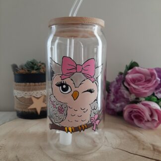 Gobelet en verre transparent avec couvercle en bambou et paille en verre, décoré d'une illustration peinte à la main d'une chouette grise faisant un clin d'œil, portant un grand nœud rose et posée sur une branche fleurie, artisanat Aleco.