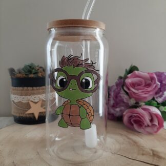 Gobelet en verre transparent avec couvercle en bambou et paille en verre, décoré d'une illustration peinte à la main d'une petite tortue verte portant de grandes lunettes rondes marron et ayant une petite mèche de cheveux, artisanat Aleco.