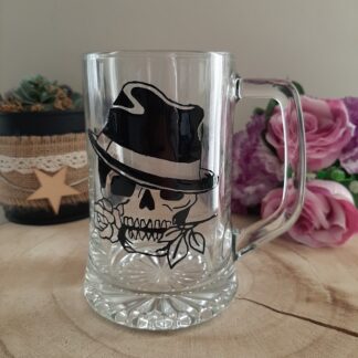Grande chope à bière en verre transparent avec anse, décorée d'une illustration noire peinte à la main représentant un crâne portant un chapeau de type fedora et tenant une rose entre ses dents, artisanat Aleco.