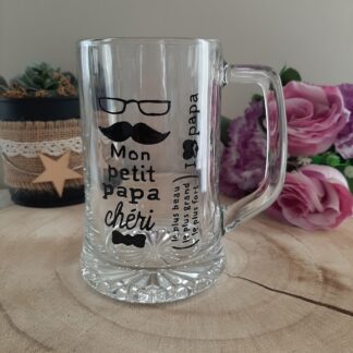 chope à bière en verre transparent avec anse, décorée d'une illustration noire peinte à la main comprenant des lunettes, une moustache, un nœud papillon et les inscriptions "Mon petit papa chéri", "I ❤️ PAPA" et "le plus beau, le plus grand, le plus fort", artisanat Aleco.