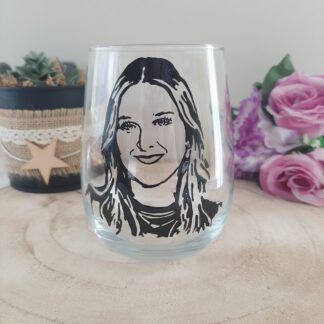 Verre gobelet arrondi transparent peint à la main levée avec une illustration noire représentant le portrait de la chanteuse Héléna, présenté sur un support en bois