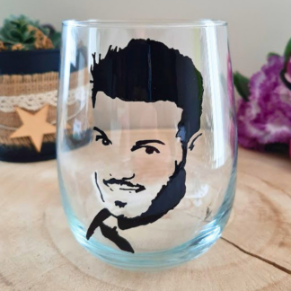 Verre gobelet arrondi transparent peint à la main levée avec une illustration noire représentant le portrait de profil du chanteur M. Pokora, présenté sur un support en bois