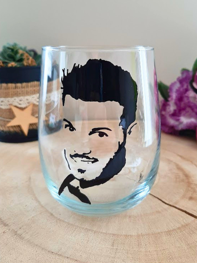 Verre gobelet arrondi transparent peint à la main levée avec une illustration noire représentant le portrait de profil du chanteur M. Pokora, présenté sur un support en bois