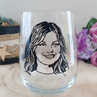 Verre gobelet arrondi transparent peint à la main levée avec une illustration noire représentant le visage et le portrait souriant de Marine de la Star Academy, présenté sur un support en bois