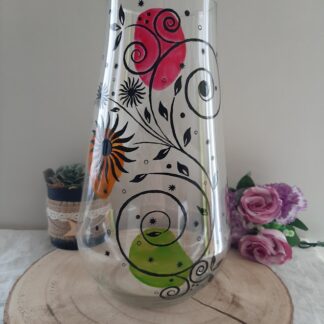 Grand vase transparent de 30 cm peint à la main avec des fleurs colorées rose, orange, vert et des volutes noires.