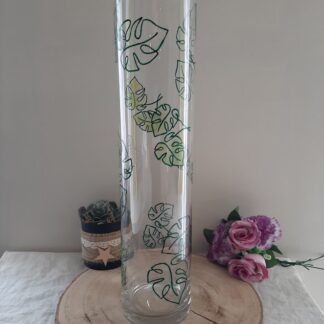 Grand vase cylindrique transparent décoré de feuilles de Monstera vertes peintes à la main.