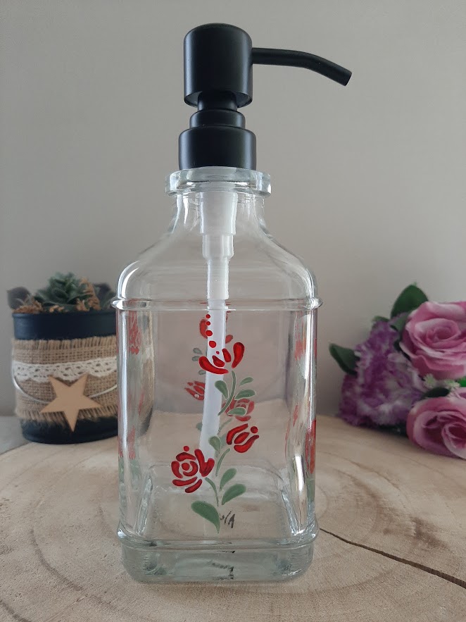 Flacon distributeur de savon en verre avec pompe noire, décoré de roses rouges et de feuilles vertes peintes à la main.
