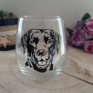 Verre transparent avec un portrait de chien Labrador peint à la main en noir, posé sur un support en bois rond.