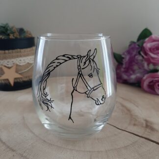 Verre transparent montrant un profil de tête de cheval peint à la main avec une crinière tressée, posé sur un support bois.