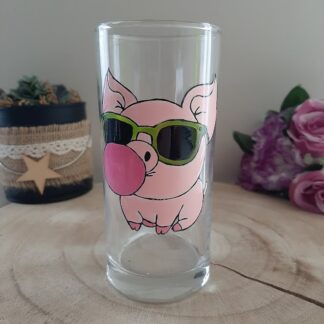 Verre haut transparent avec un dessin de petit cochon rose portant des lunettes de soleil vertes et faisant une bulle de chewing-gum rose.