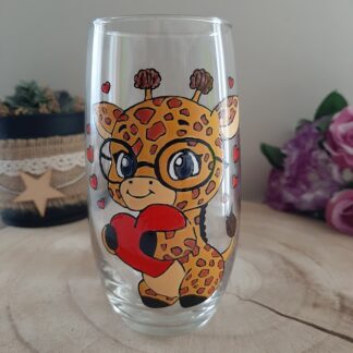 Verre transparent galbé avec une girafe à lunettes tenant un cœur rouge, peinte à la main avec de petits cœurs autour.