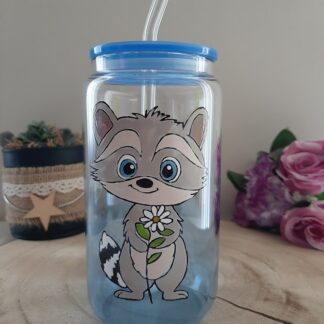 Verre canette transparent avec un raton laveur tenant une fleur peint à la main, couvercle bleu et paille en verre.