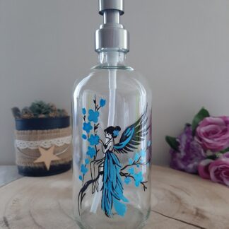 Distributeur de savon en verre avec peinture artisanale d'une fée aux ailes bleues assise sur une branche fleurie.