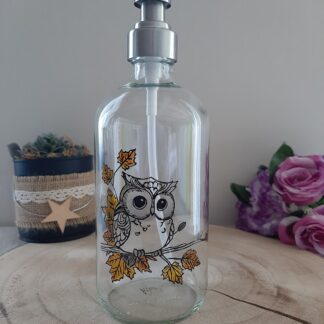 Distributeur de savon en verre avec peinture artisanale d'une chouette aux grands yeux sur une branche de feuilles d'automne orangées.