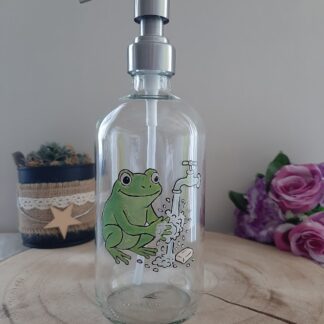 Distributeur de savon en verre avec décor d'une grenouille verte se lavant les mains sous un robinet, peint à la main.