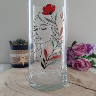 Vase cylindrique en verre de 20 cm de haut, peint à la main avec une illustration en Line Art d'un visage de femme et un coquelicot rouge, posé sur un socle en bois