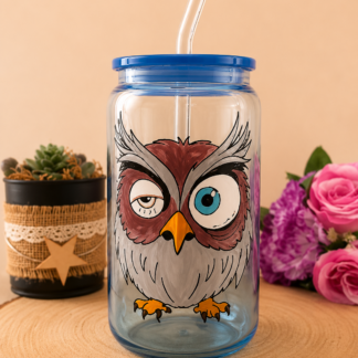 Verre en forme de canette bleu avec couvercle et paille, peint à la main avec un hibou rigolo aux yeux asymétriques, posé sur un support en bois
