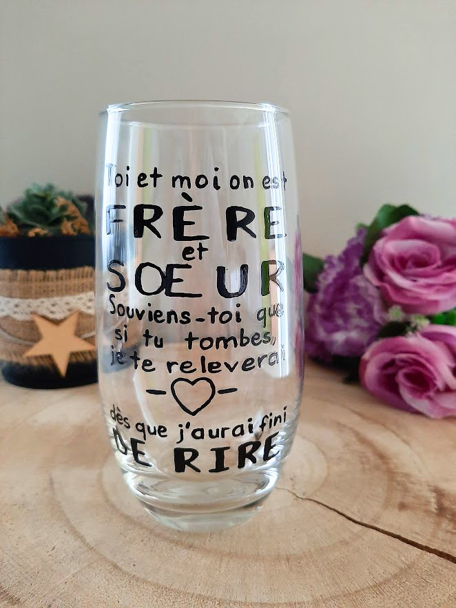 Verre haut transparent peint à la main levée avec une citation humoristique noire sur les frères et sœurs et un petit cœur, présenté sur un support en bois