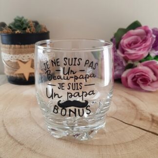 Verre taillé à message peint à la main « Je ne suis pas un Beau-papa je suis un Papa Bonus » avec moustache décorative, posé sur une rondelle de bois avec des roses en arrière plan