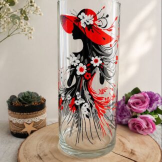 Vase décoratif de 30cm peint à la main représentant une silhouette féminine avec grand chapeau rouge et robe de fleurs blanches, posé sur une rondelle de bois