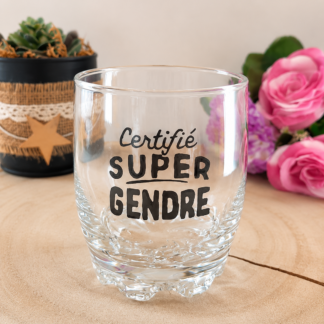 Verre taillé à message peint à la main « Certifié Super Gendre » avec typographie mixte script et majuscules, posé sur une rondelle de bois avec des roses en arrière plan