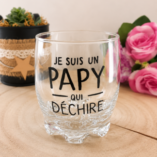 Verre taillé à message peint à la main « Je suis un Papy qui Déchire » posé sur une rondelle de bois avec des roses roses en arrière plan