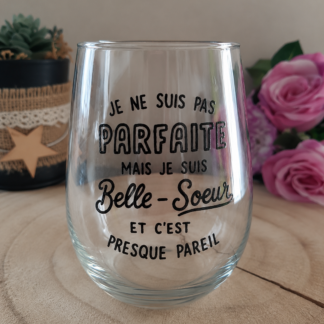 Verre à message humoristique peint à la main « Je ne suis pas Parfaite mais je suis Belle-Sœur et c'est presque pareil » posé sur une rondelle de bois avec des roses roses en arrière plan