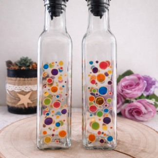 Duo huilier et vinaigrier en verre peints à la main avec pois multicolores, posés sur une table en bois avec des roses roses