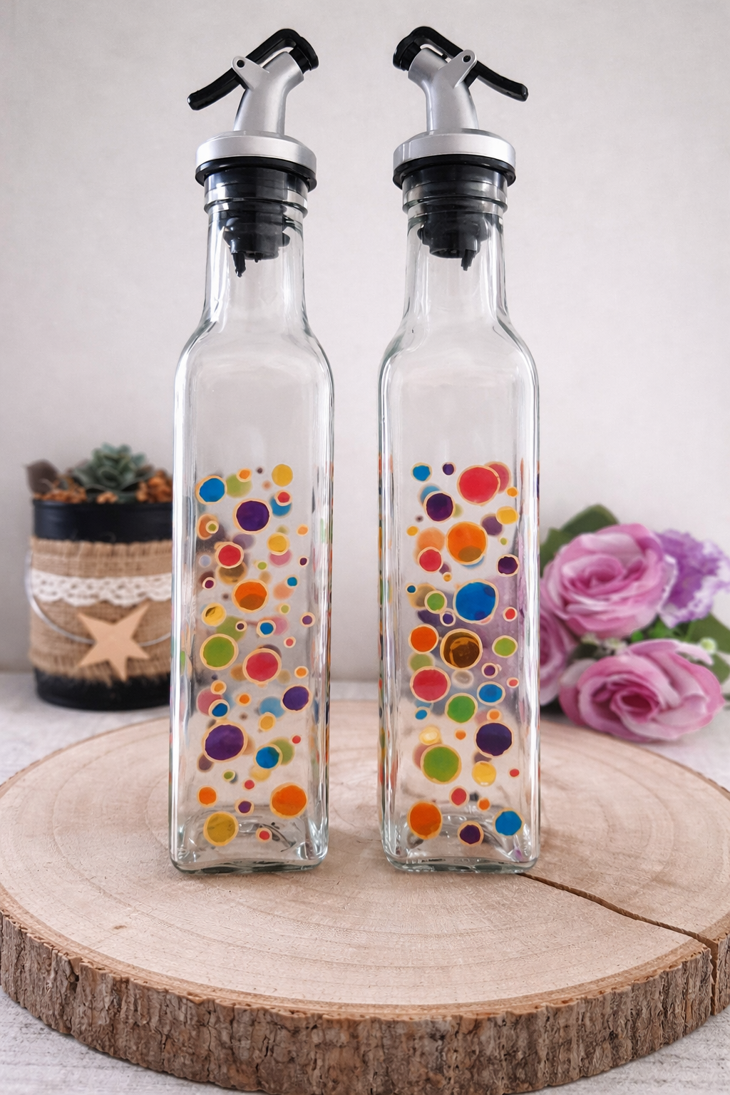 Duo huilier et vinaigrier en verre peints à la main avec pois multicolores, posés sur une table en bois avec des roses roses