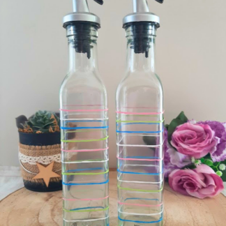 Duo huilier et vinaigrier en verre peints à la main avec rayures multicolores rose bleu vert et blanc, posés sur une table en bois avec des roses roses