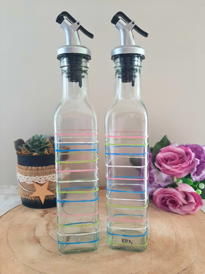Duo huilier et vinaigrier en verre peints à la main avec rayures multicolores rose bleu vert et blanc, posés sur une table en bois avec des roses roses