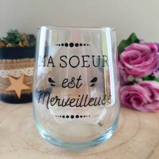 Gobelet en verre peint à la main avec inscription calligraphiée "Ma sœur est merveilleuse" et petits oiseaux noirs, posé sur une table en bois avec des roses roses