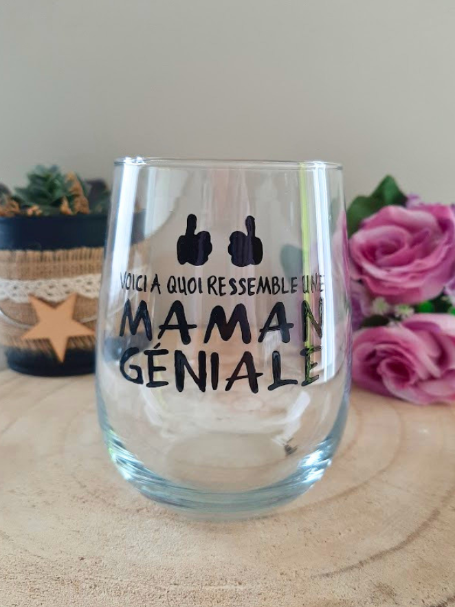 Gobelet en verre peint à la main avec inscription "Voici à quoi ressemble une maman géniale" et deux pouces levés noirs, posé sur une table en bois avec des roses roses