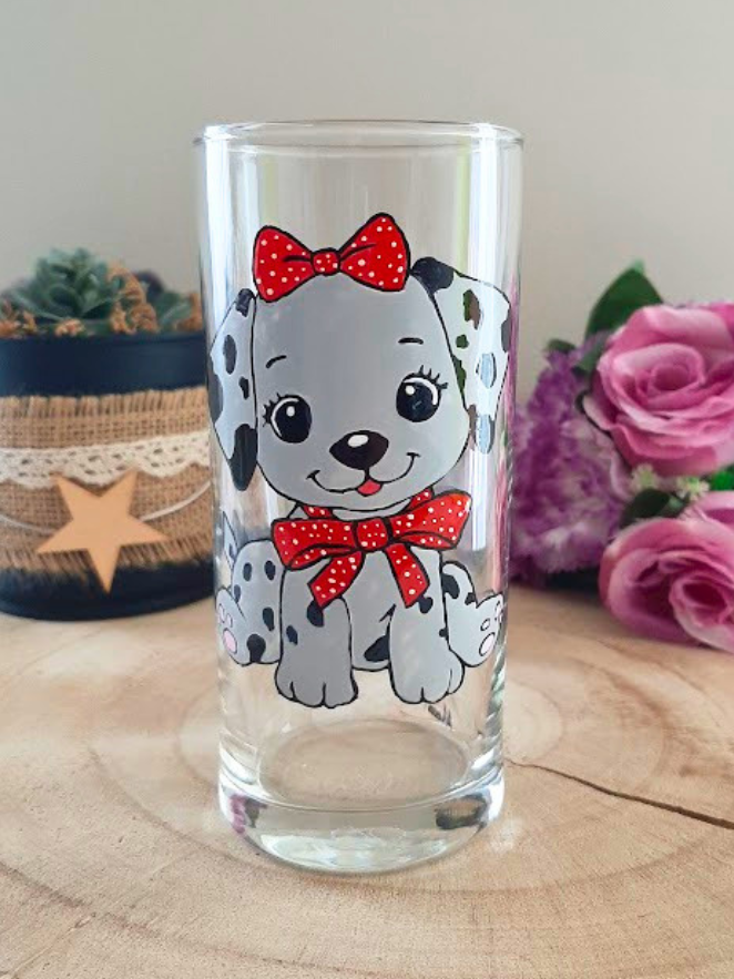 Verre droit peint à la main avec chiot dalmatien et nœuds rouges à pois, posé sur une table en bois avec des roses roses
