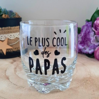 Verre à whisky peint à la main avec inscription "Le plus cool des papas", petits cœurs et étincelles, posé sur une table en bois avec des roses roses