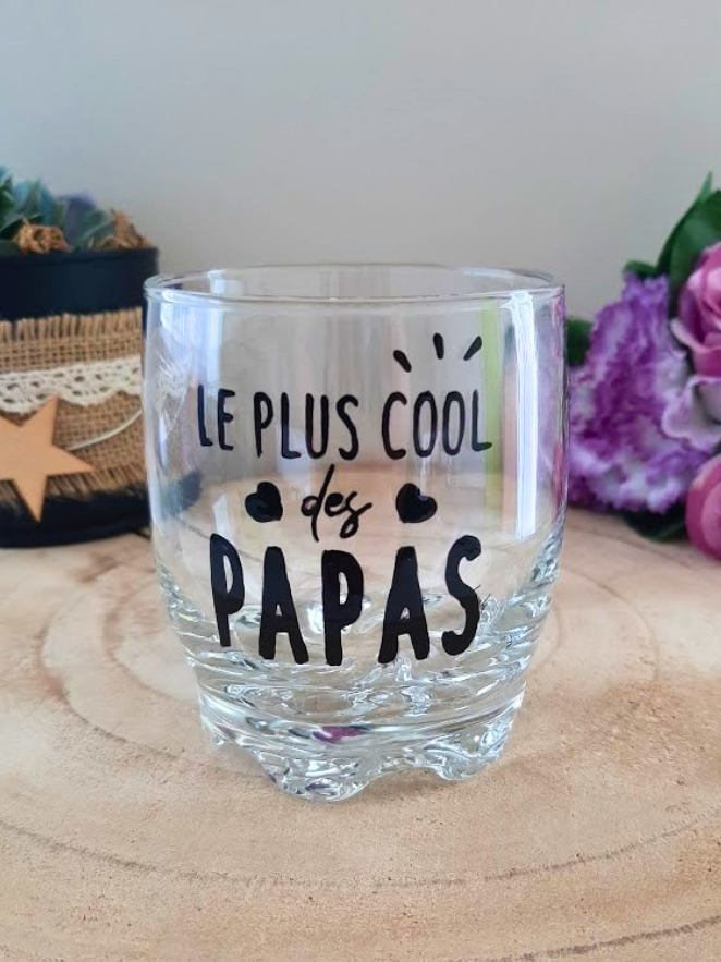Verre à whisky peint à la main avec inscription "Le plus cool des papas", petits cœurs et étincelles, posé sur une table en bois avec des roses roses