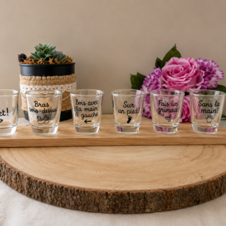 Coffret de 6 verres à shot peints à la main avec gages et défis (Un secret, Bras dessus-dessous, Sur un pied...), présentés sur leur planchette en bois sur une table en bois