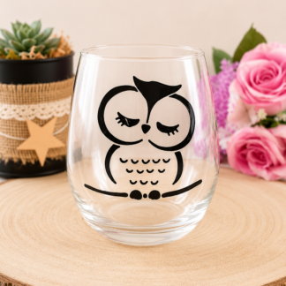 Gobelet en verre peint à la main avec hibou endormi noir et blanc style graphique épuré, posé sur une table en bois avec des roses roses