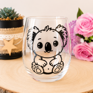 Gobelet en verre peint à la main avec koala noir et blanc style graphique épuré, posé sur une table en bois avec des roses roses