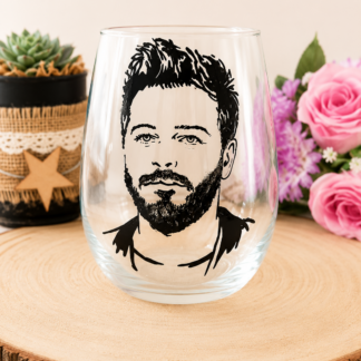 Gobelet en verre peint à la main avec portrait réaliste de Christophe Maé en noir et blanc, posé sur une table en bois avec des roses roses