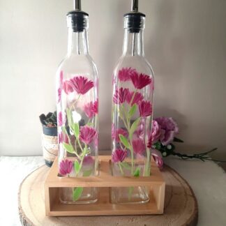 Duo huilier et vinaigrier en verre peints à la main avec grandes fleurs roses et feuillage vert, présentés dans leur support en bois naturel sur une table en bois