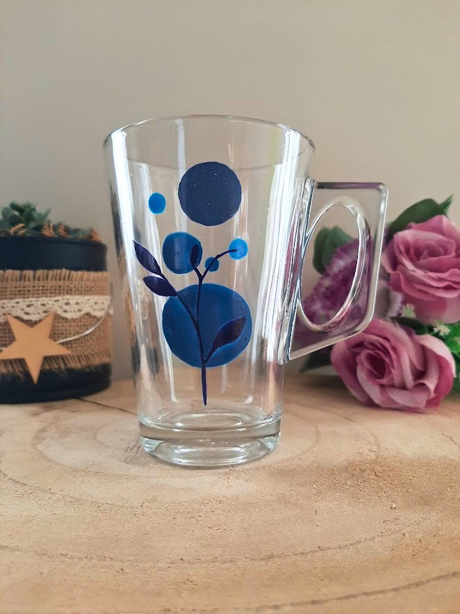 Mug en verre peint à la main avec fleur bleue abstraite composée de ronds, posé sur une table en bois