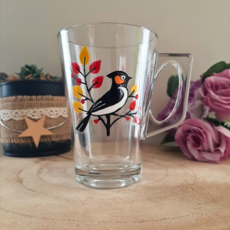 Mug en verre peint à la main avec oiseau sur une branche et feuilles d'automne, posé sur une table en bois
